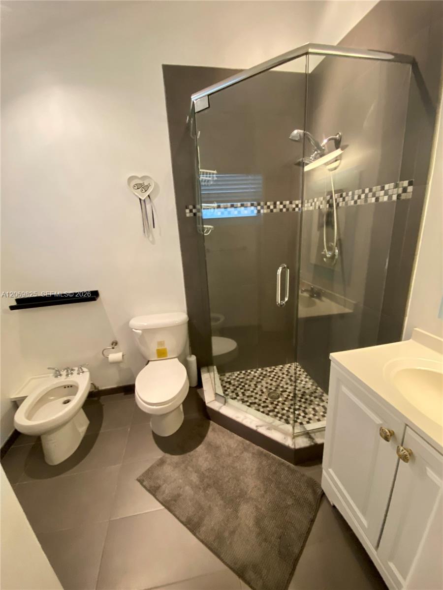 Bathroom with a glass corner shower, mosaic tile accents, toilet, bidet, and white vanity.