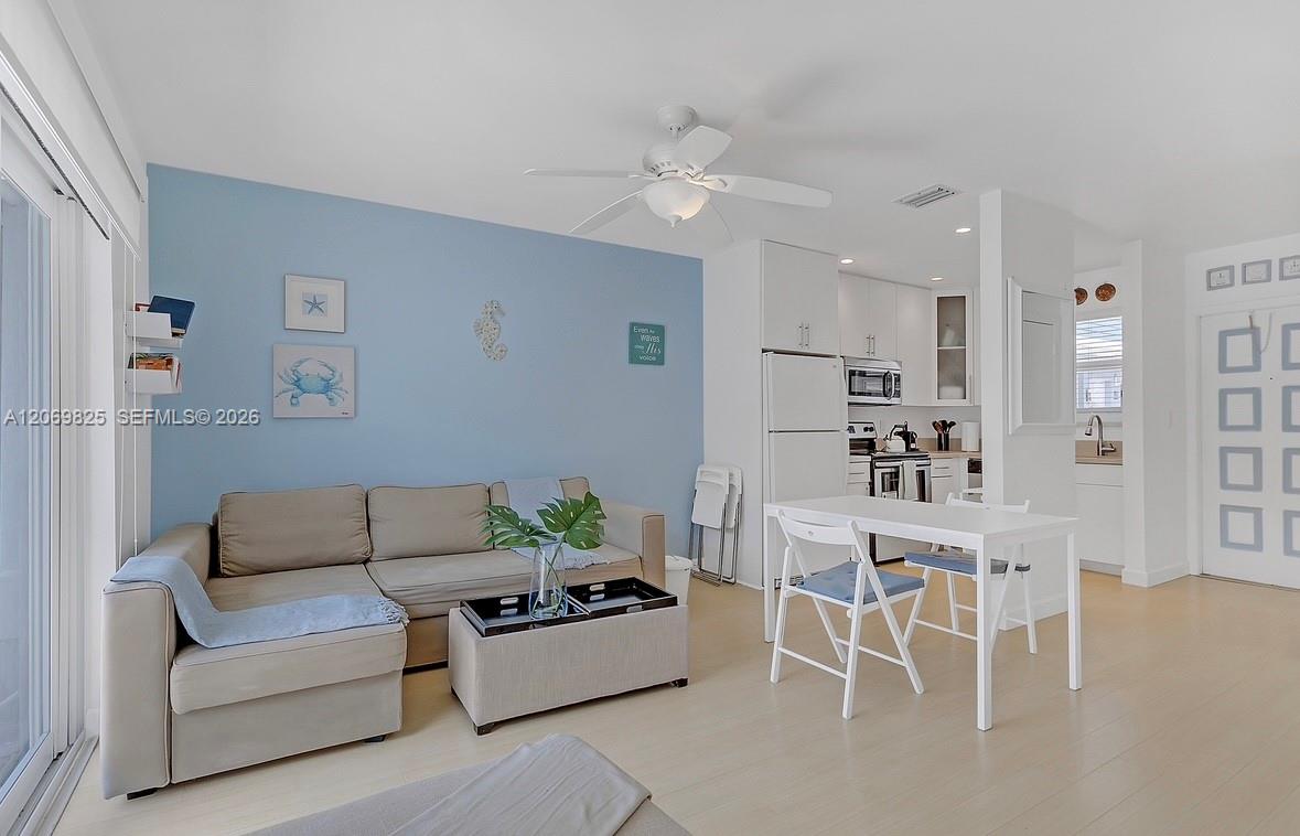 Open-plan living room and kitchen with a beige sectional, blue accent wall, and white dining table.