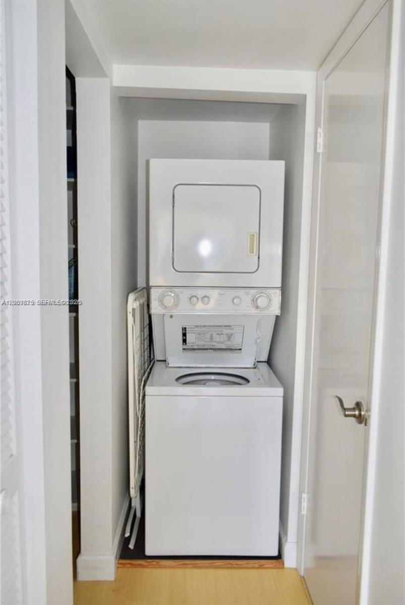 Stacked washer and dryer in a narrow closet, with a folding ironing board stored alongside.