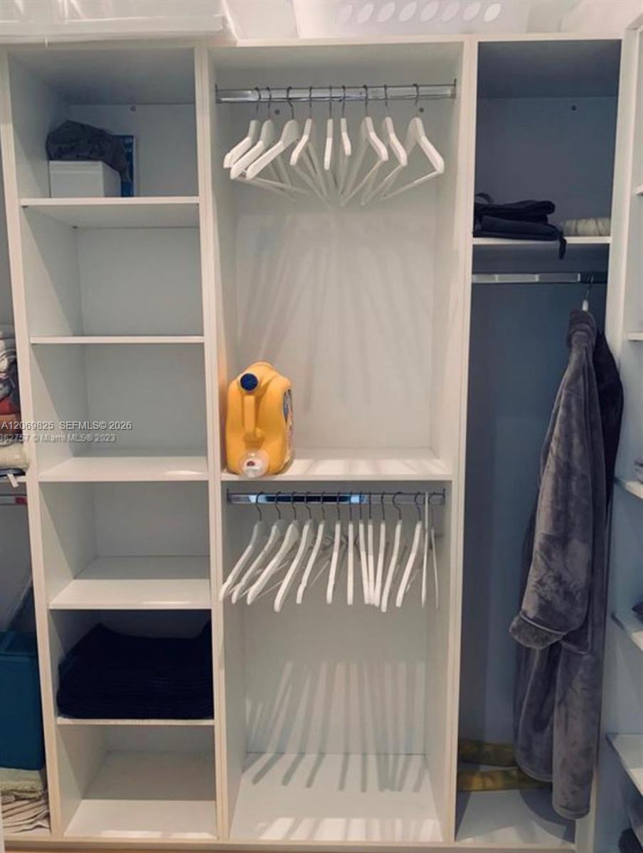 Walk-in closet with white built-in shelving, rows of hangers, folded clothes, and a hanging gray robe.