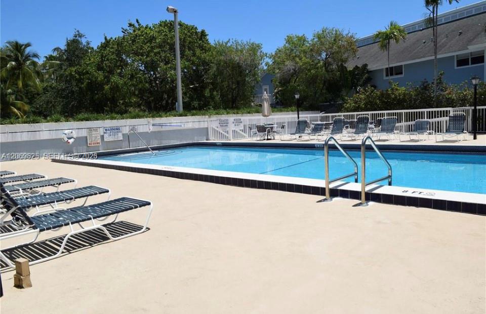 Condominium pool with lounge chairs, metal entry rails, and tropical landscaping.