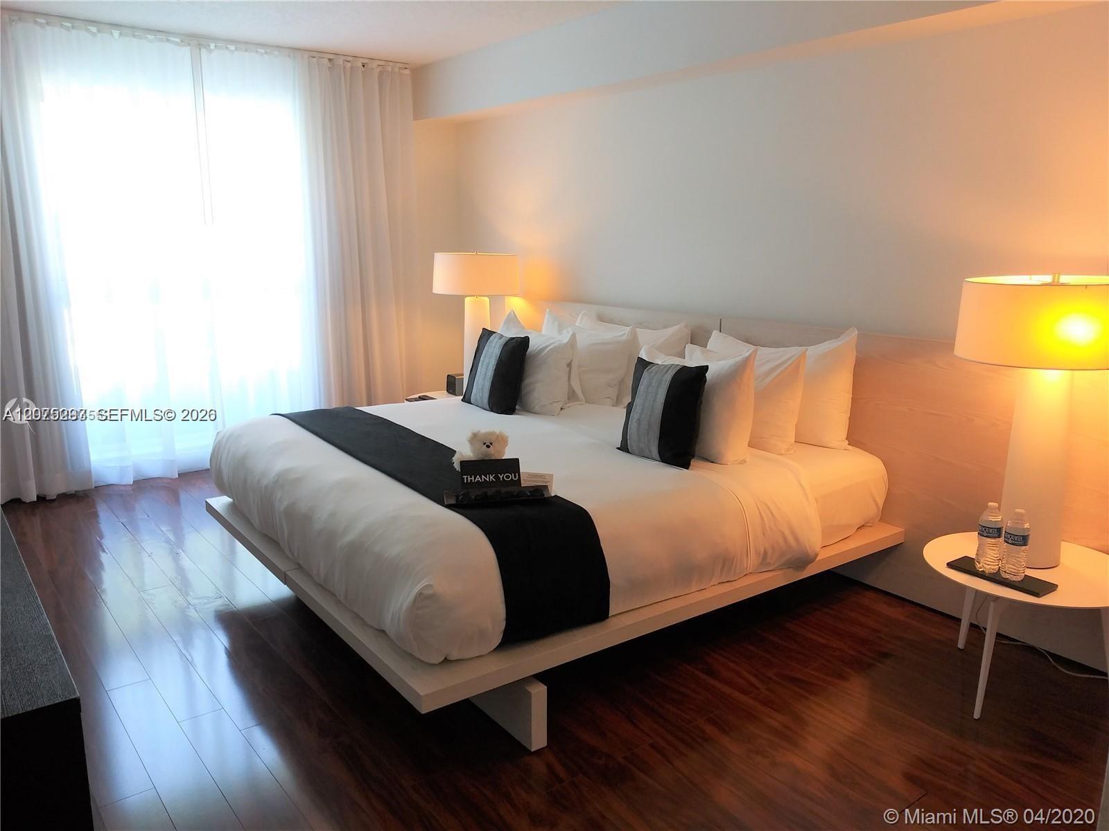 Bedroom with a white bed, black accents, dark wood flooring, and a bright curtained window.