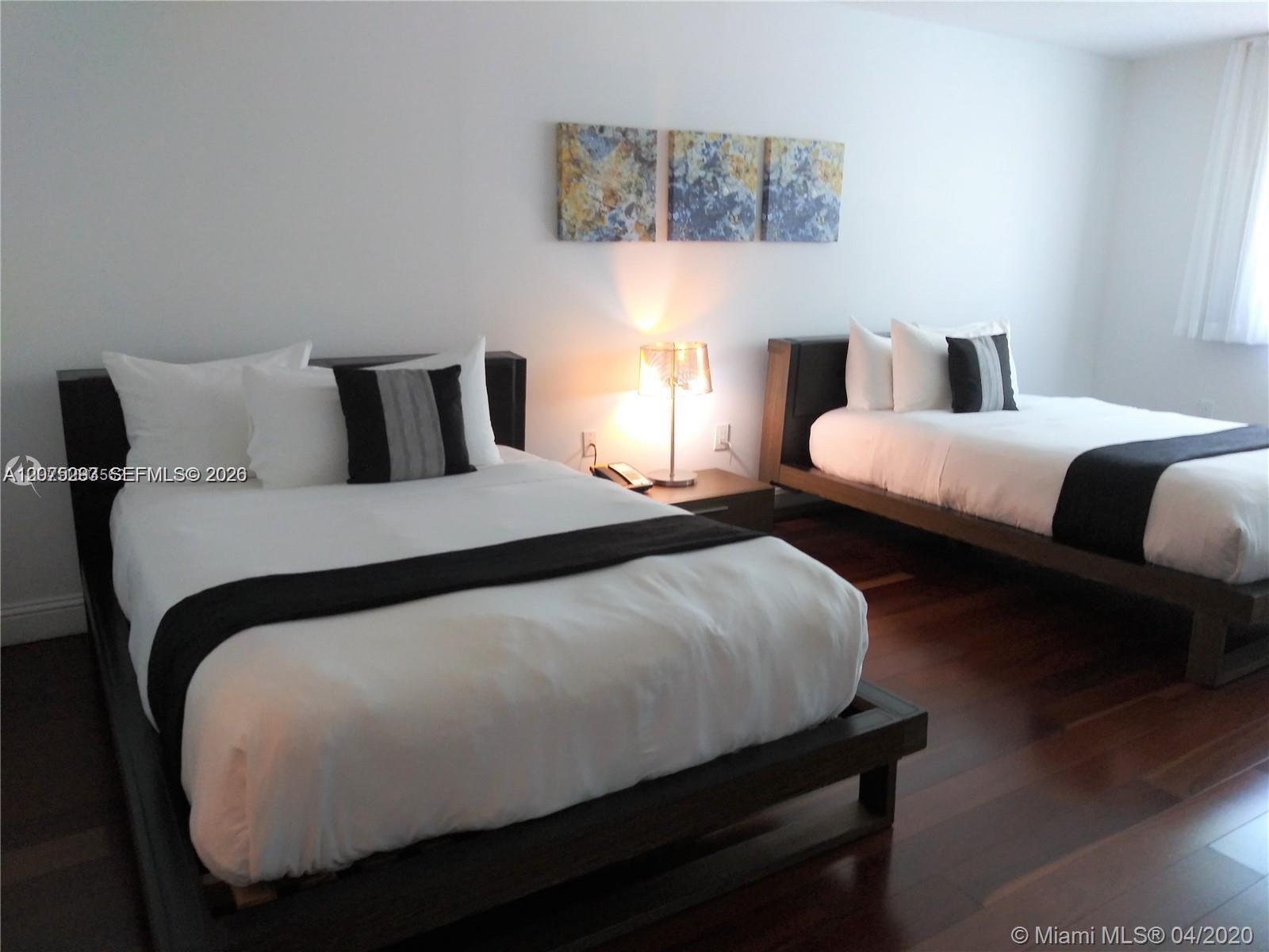 Bedroom with two platform beds, white bedding, dark accents, and a lit lamp between them.