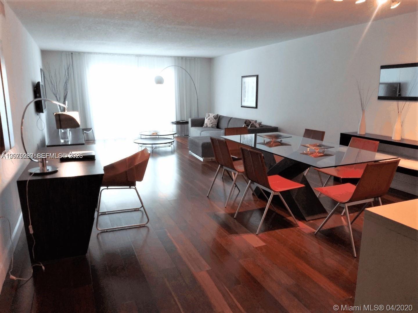 Furnished living and dining room with dark wood floors, a glass table, reddish-brown chairs, and gray sofa.