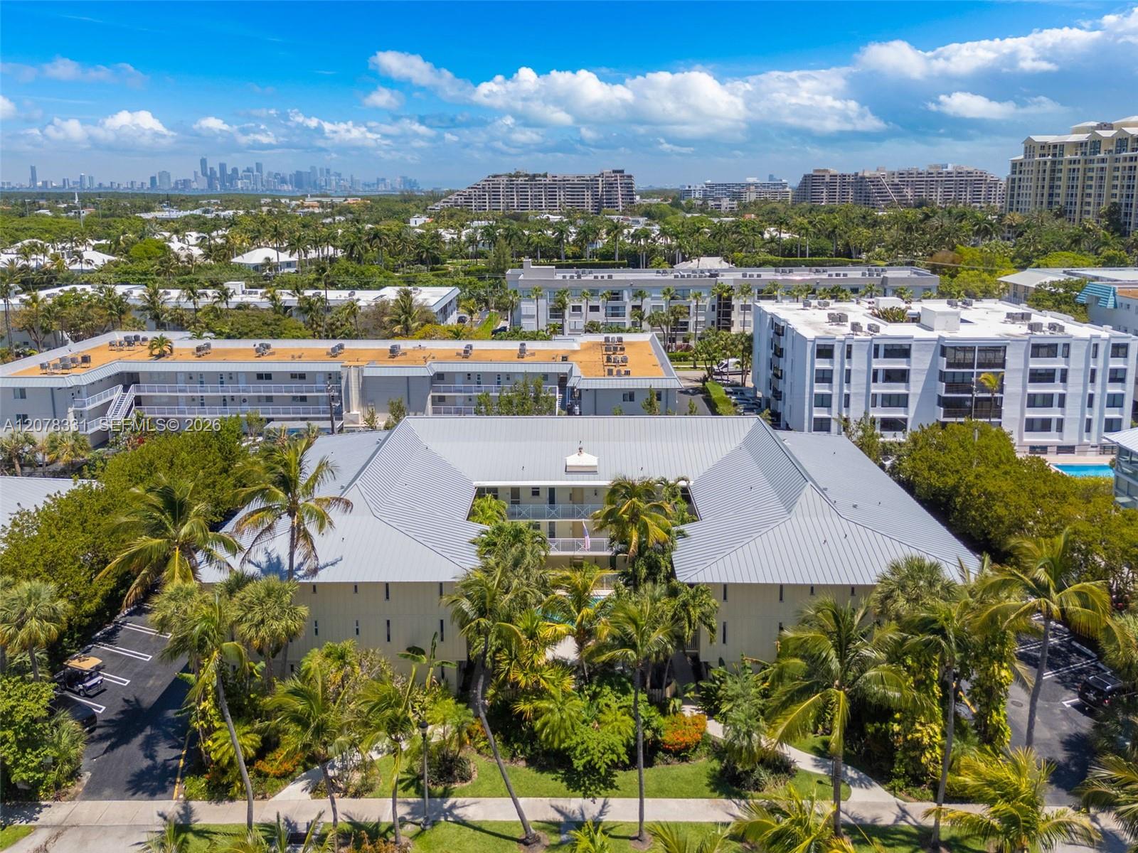 Aerial view of the condominium complex, palm-lined grounds, and Miami skyline in the distance.