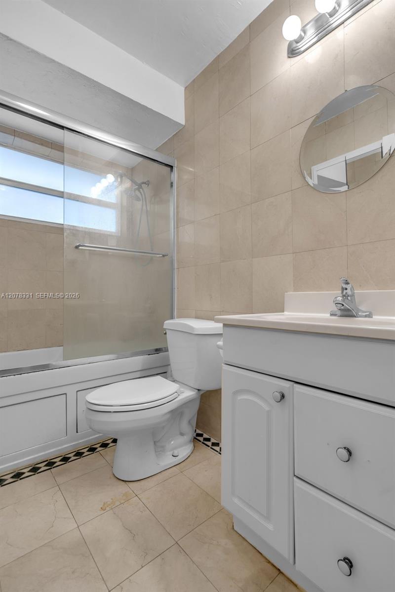 Bathroom with a glass-enclosed shower, white toilet, and vanity against beige tile.