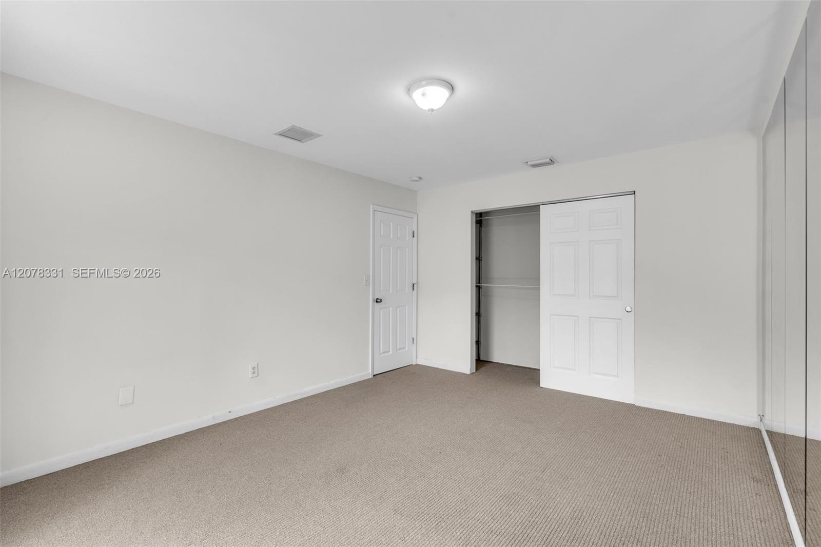 Empty bedroom with beige carpet, an open closet, and mirrored closet doors.