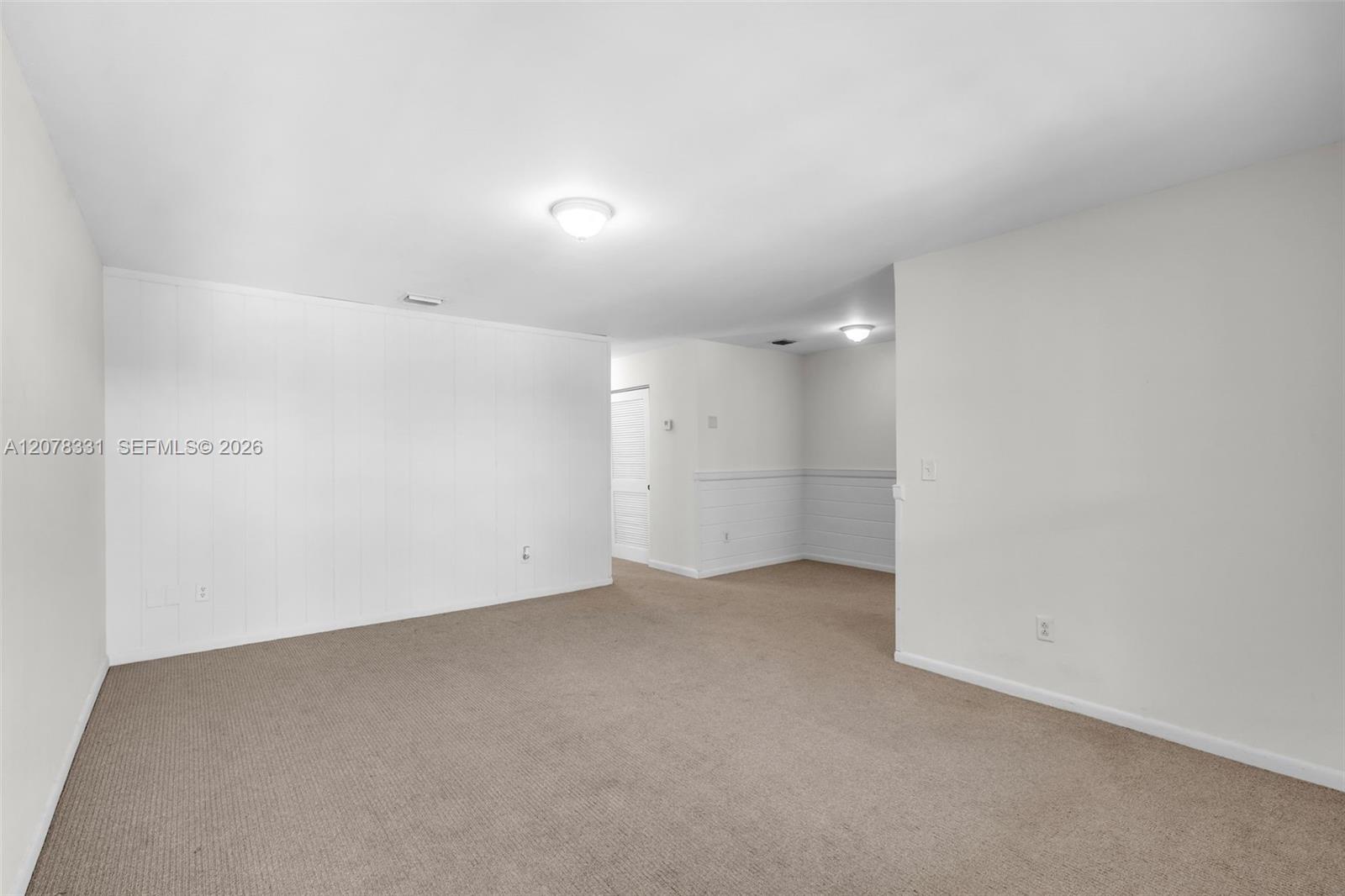 Empty carpeted room with white paneled walls and a louvered closet door.