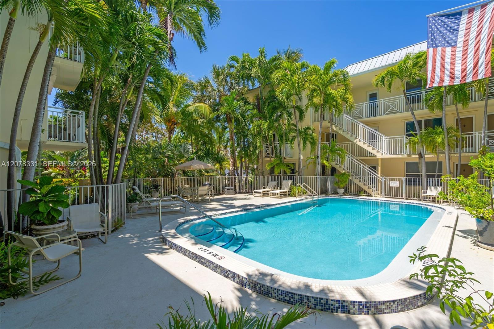 Condominium courtyard pool bordered by palm trees, lounge chairs, and exterior staircases.