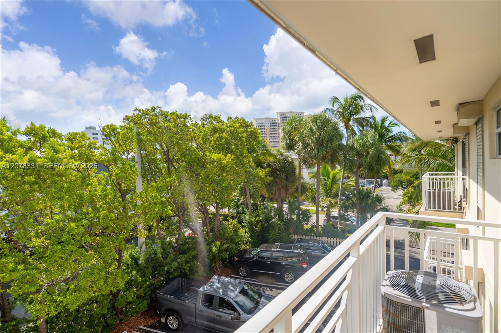 Balcony overlooking palm trees, leafy grounds, and a parking area.