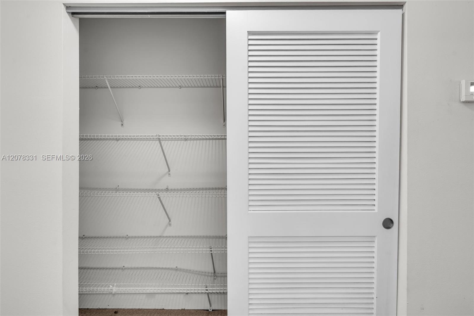 Walk-in closet with white wire shelving and a partially open louvered door.
