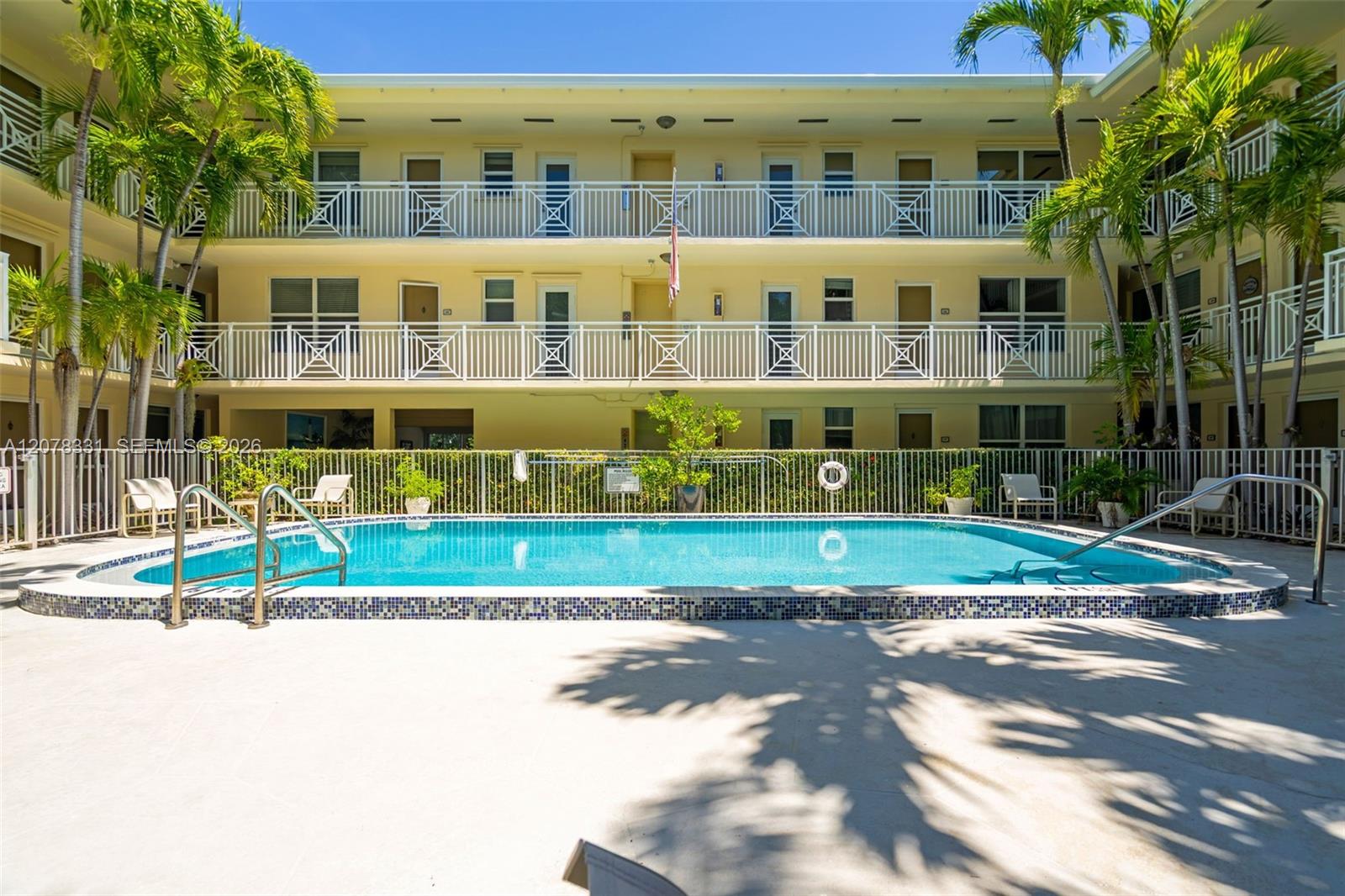 Courtyard pool in front of a yellow condominium with white balconies and palm trees.
