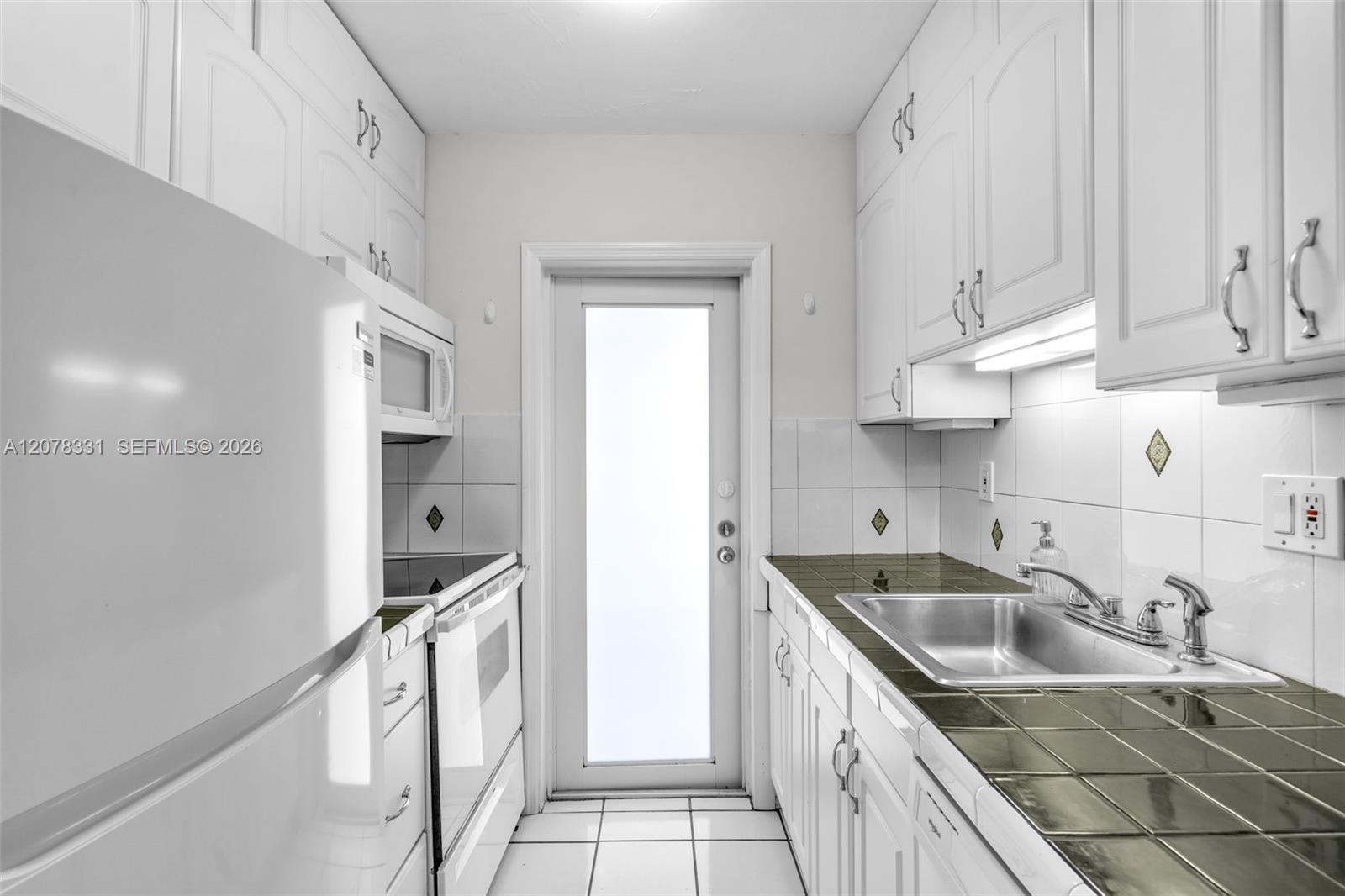 Galley kitchen with white cabinets, dark green tile countertops, and a stainless-steel double sink.