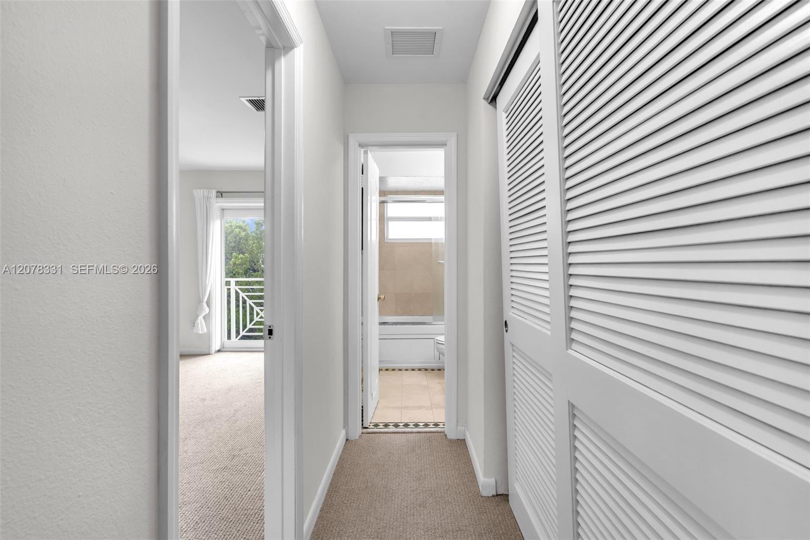 Apartment hallway with louvered closet doors, opening to a bathroom and bedroom with a balcony door.