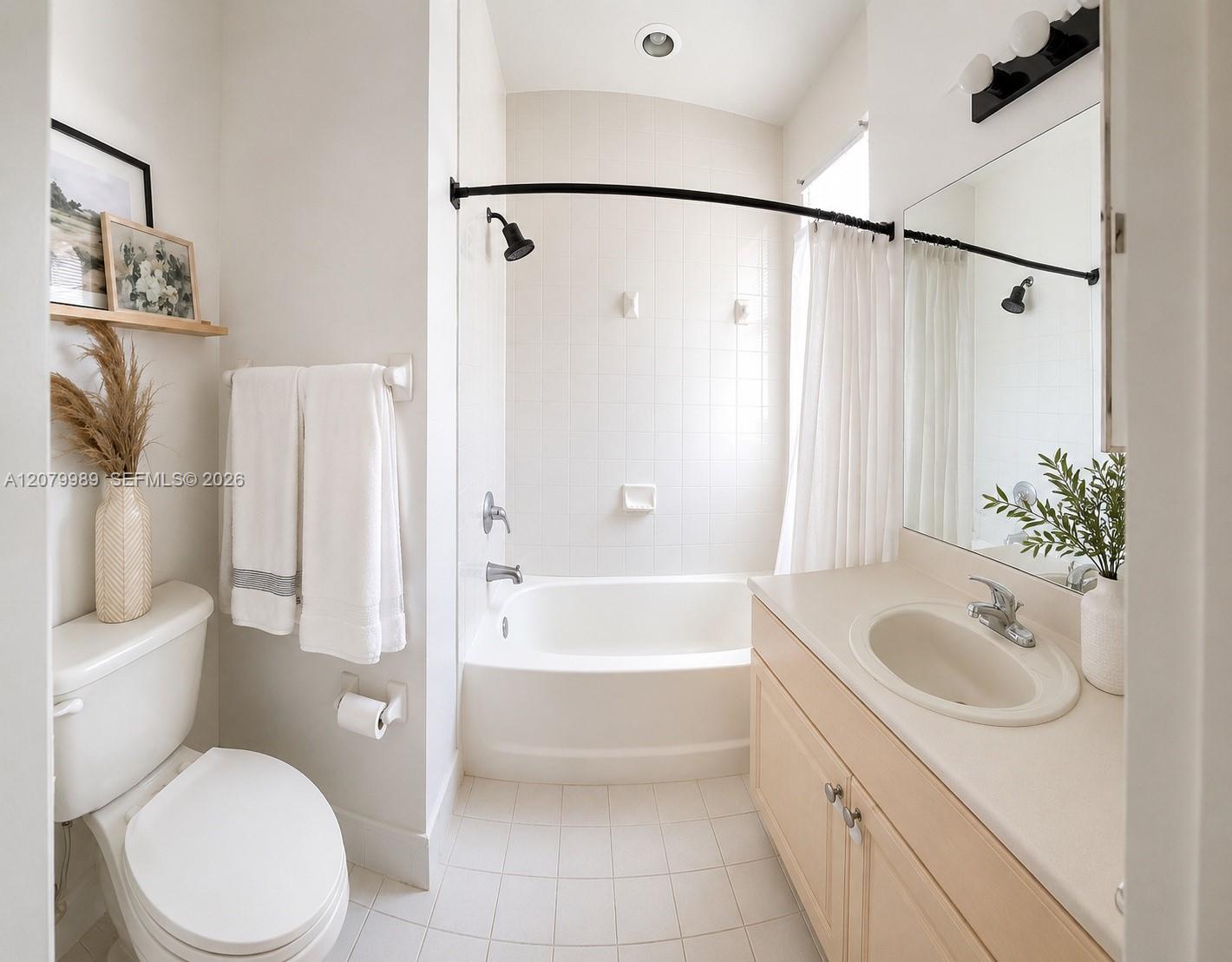 Bathroom with a white tub and shower, toilet, and light wood vanity with a large mirror.