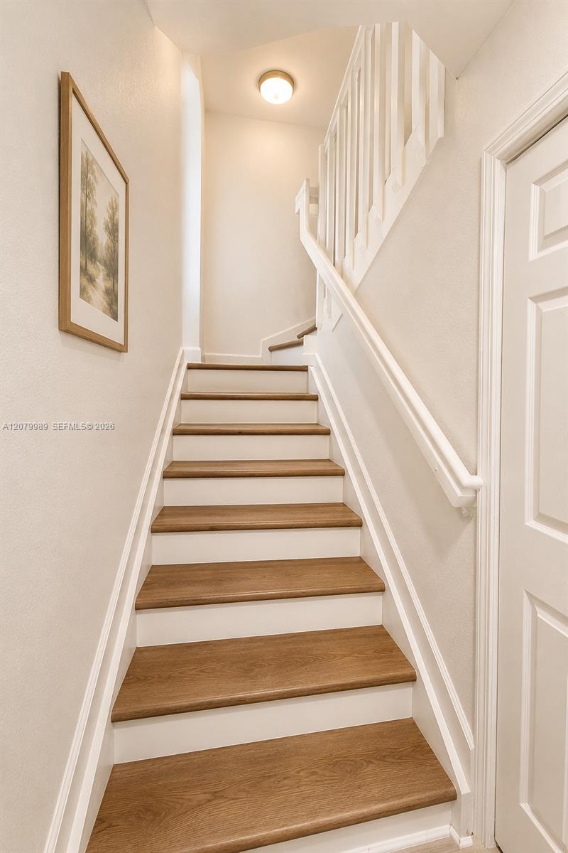 Interior staircase with wood treads, white risers and railings, framed wall art and a paneled door.