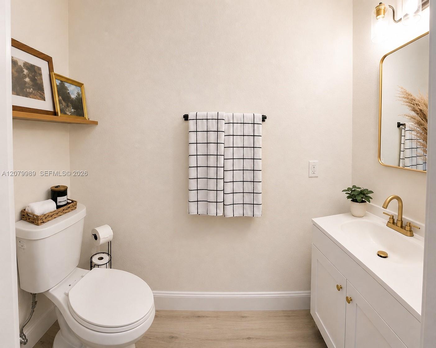 Bathroom with a white vanity, brass fixtures, and black-grid towels above a white toilet.