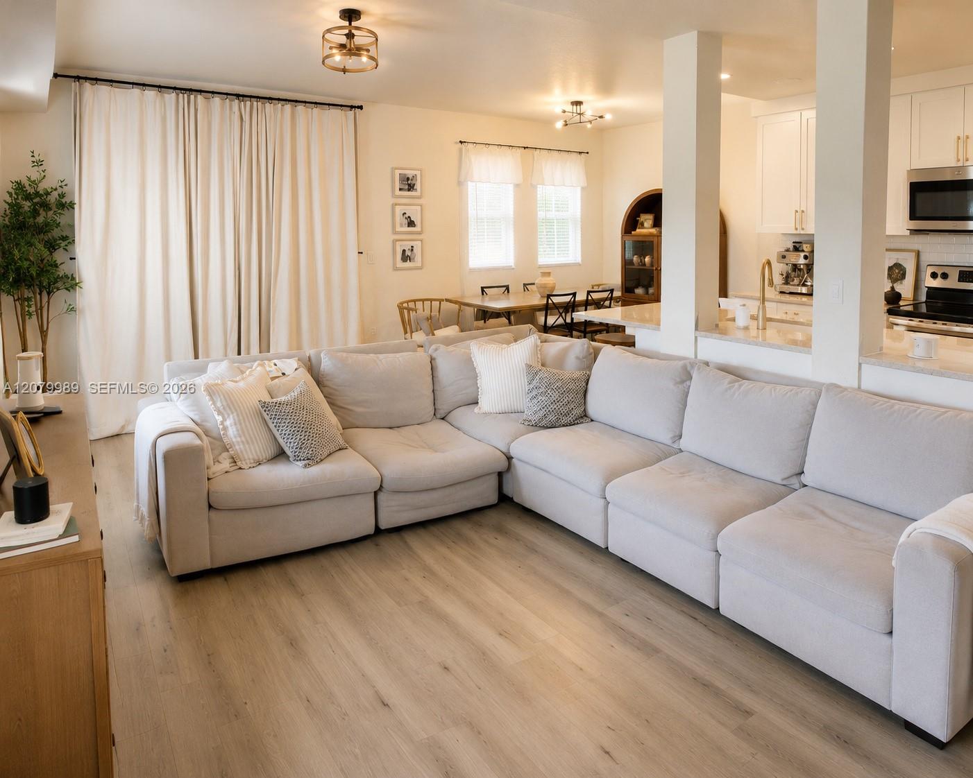 Open-plan living room with a cream sectional, light wood floors, and dining area beside the kitchen.