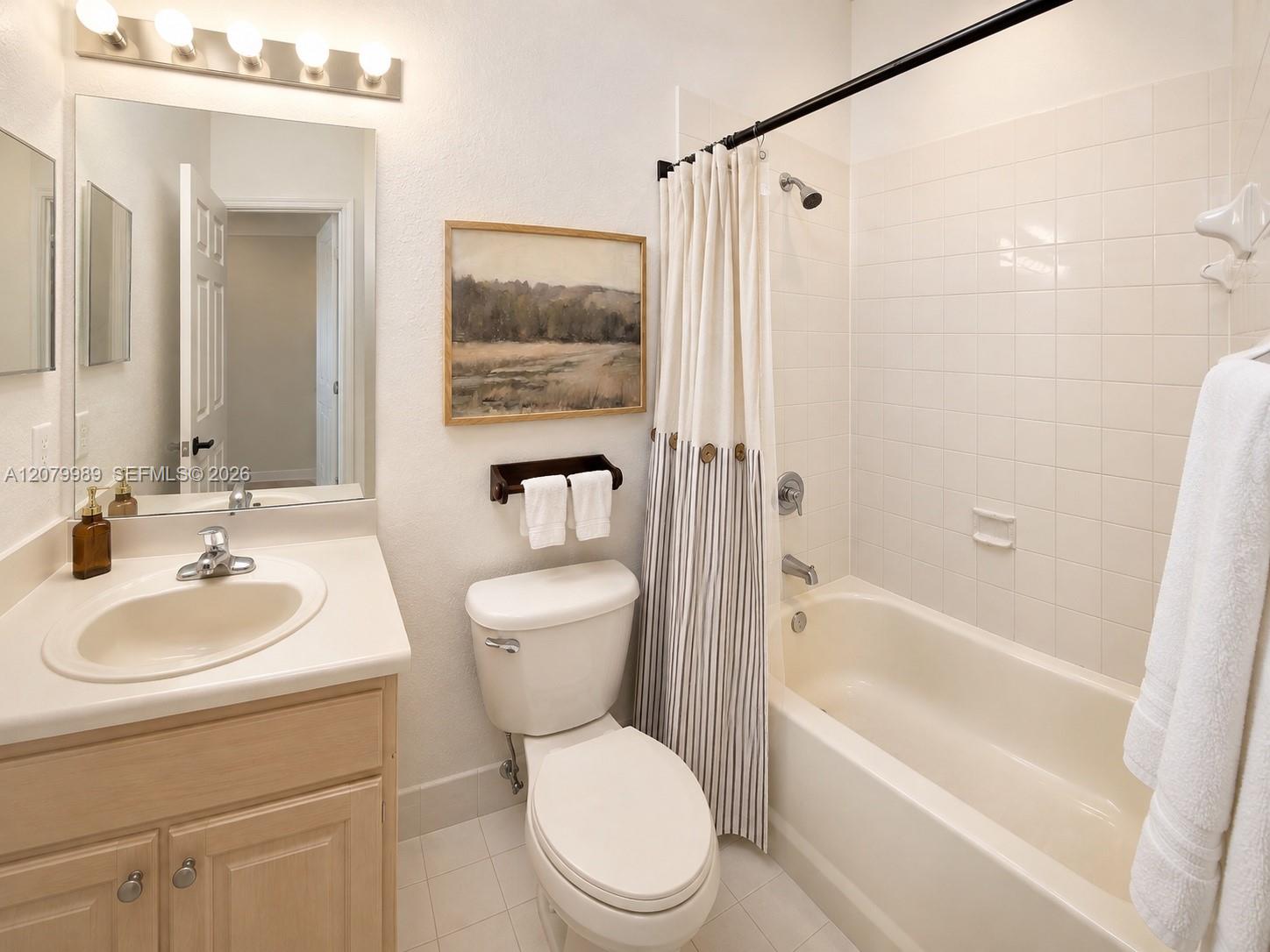 Bathroom with light wood vanity, toilet, and white tub behind a striped shower curtain.