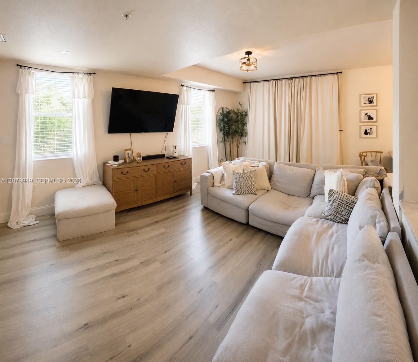 Furnished living room with a white sectional, light wood floors, and a wall-mounted television.