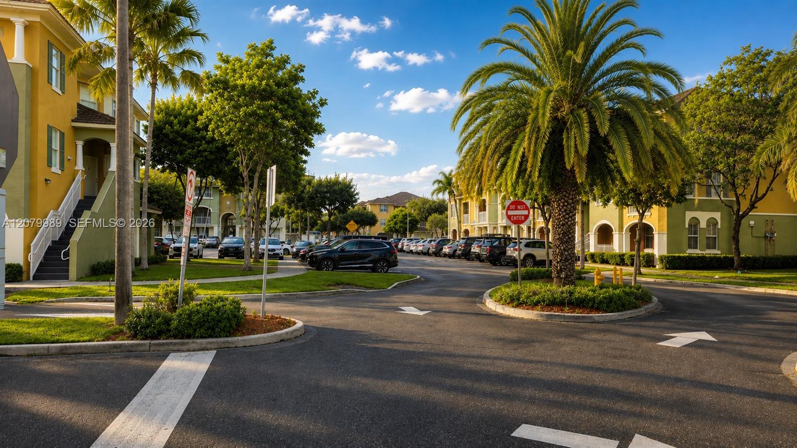 Condominium community drive lined with palm trees, parked cars, and yellow stucco buildings.