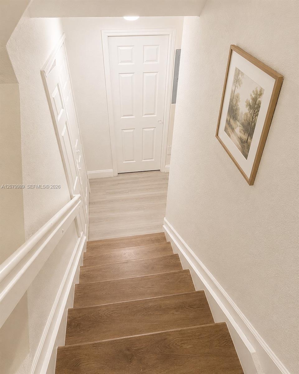 Wooden staircase with white railing descends toward a paneled door; a framed landscape print hangs nearby.