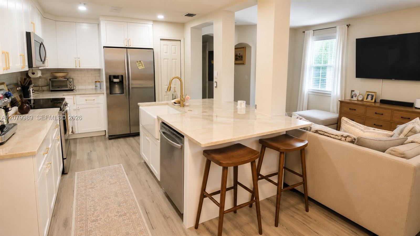 Open-plan kitchen with a large island, gold faucet, wooden stools, and adjoining beige living room.
