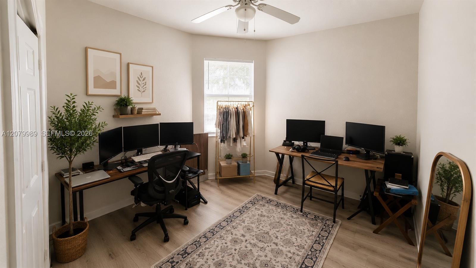 Home office with two computer workstations, a clothing rack by the window, and a patterned rug.