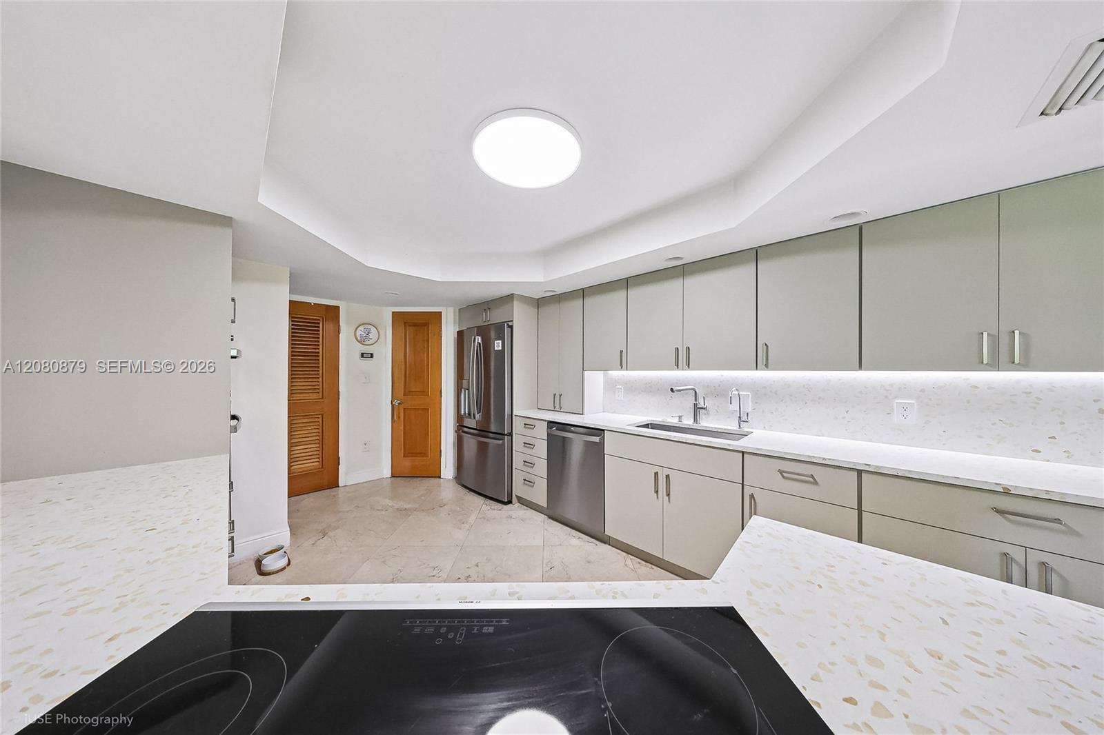 Modern kitchen with gray cabinets, white counters, stainless steel appliances, and a black induction cooktop.