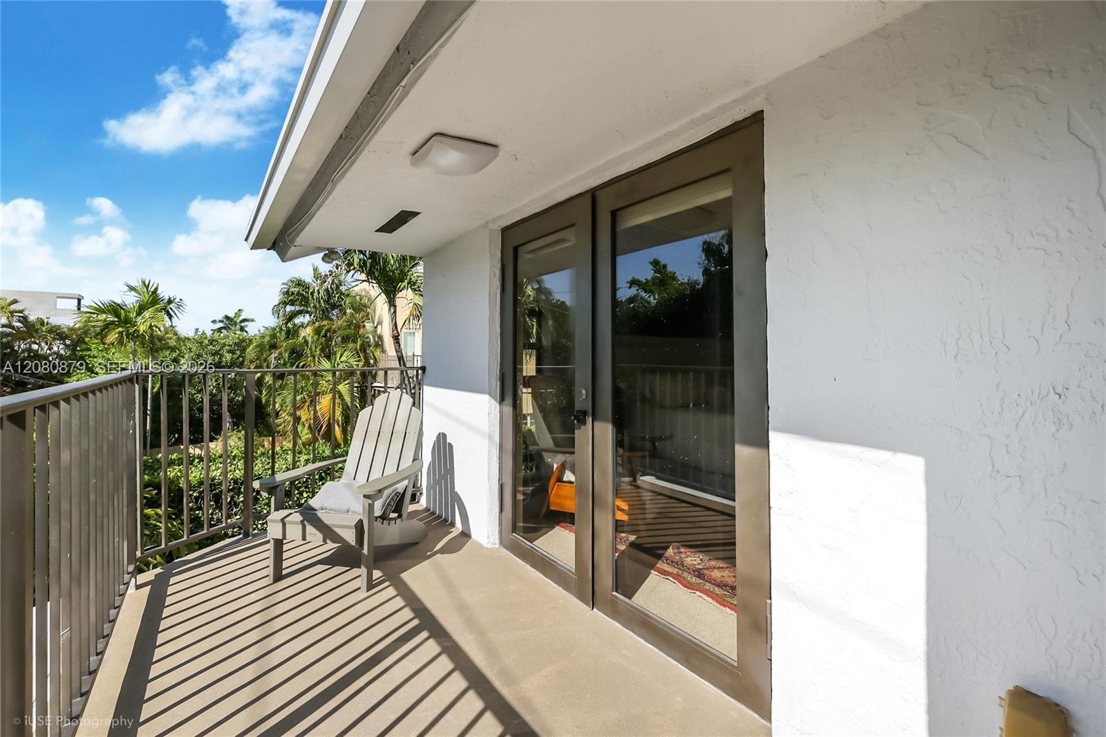 Covered balcony with a single chair, glass doors, and views of tropical greenery.