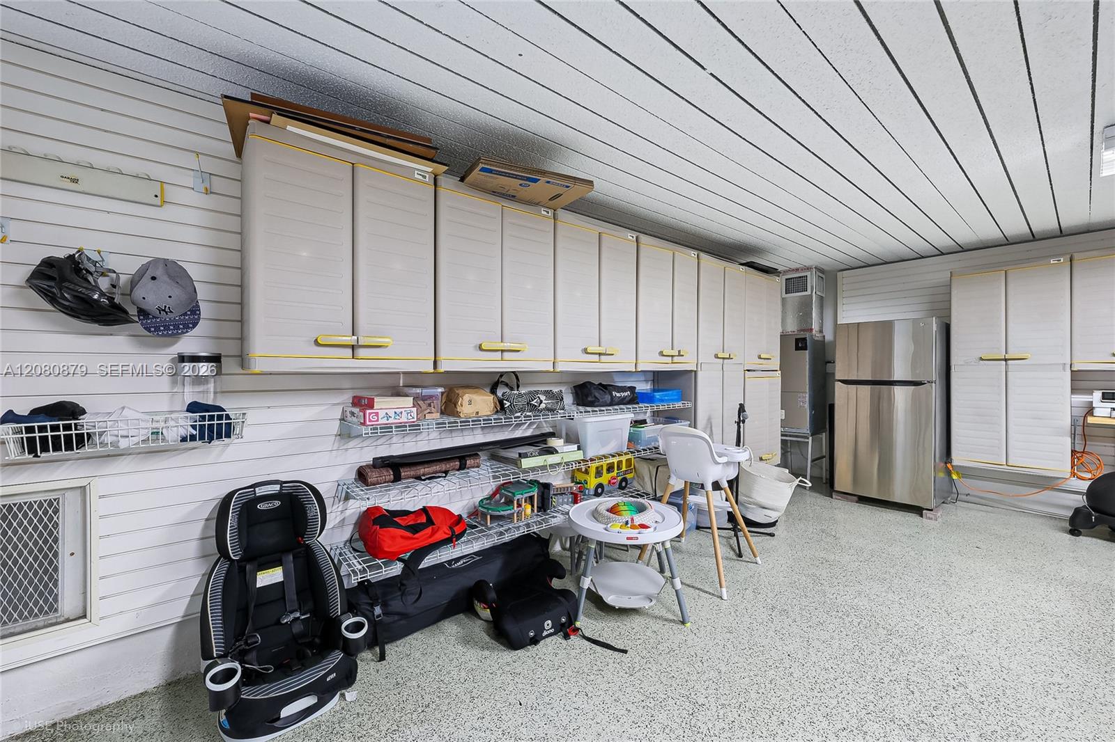 Garage storage room with white cabinets, wire shelving, and a stainless steel refrigerator.