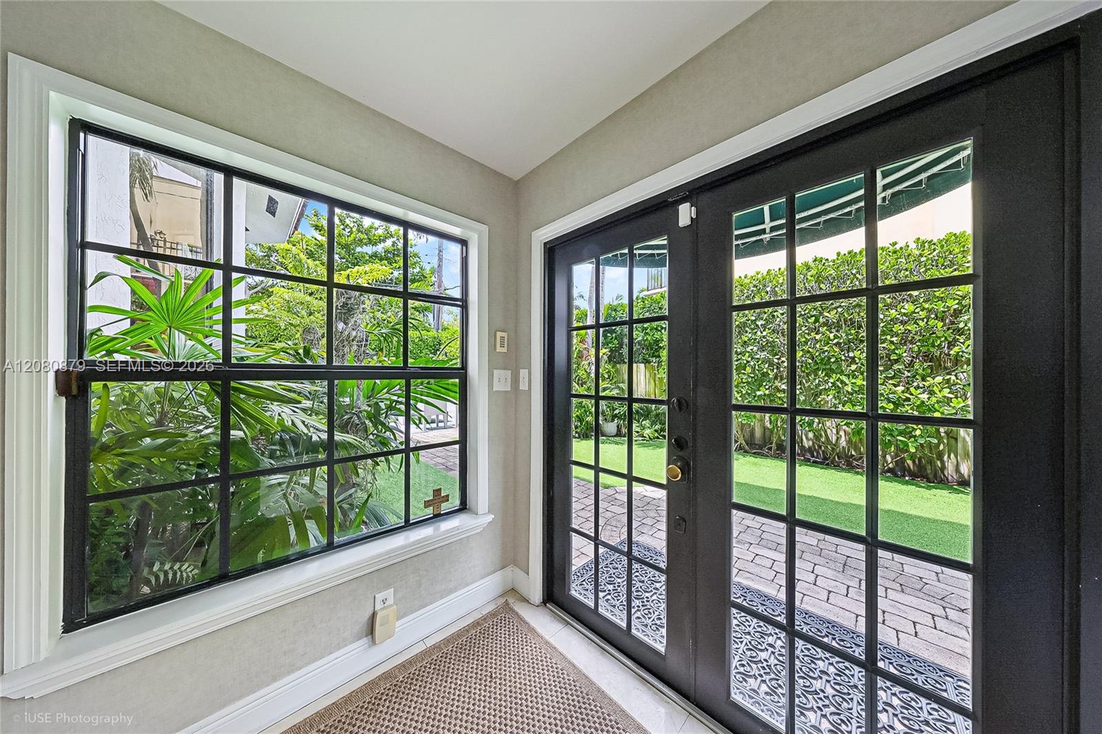 Entryway with black-framed glass doors and window overlooking a garden.