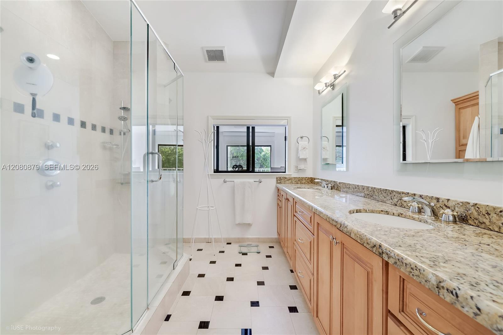 Bathroom with a glass-enclosed shower and long granite double vanity with warm wood cabinets.