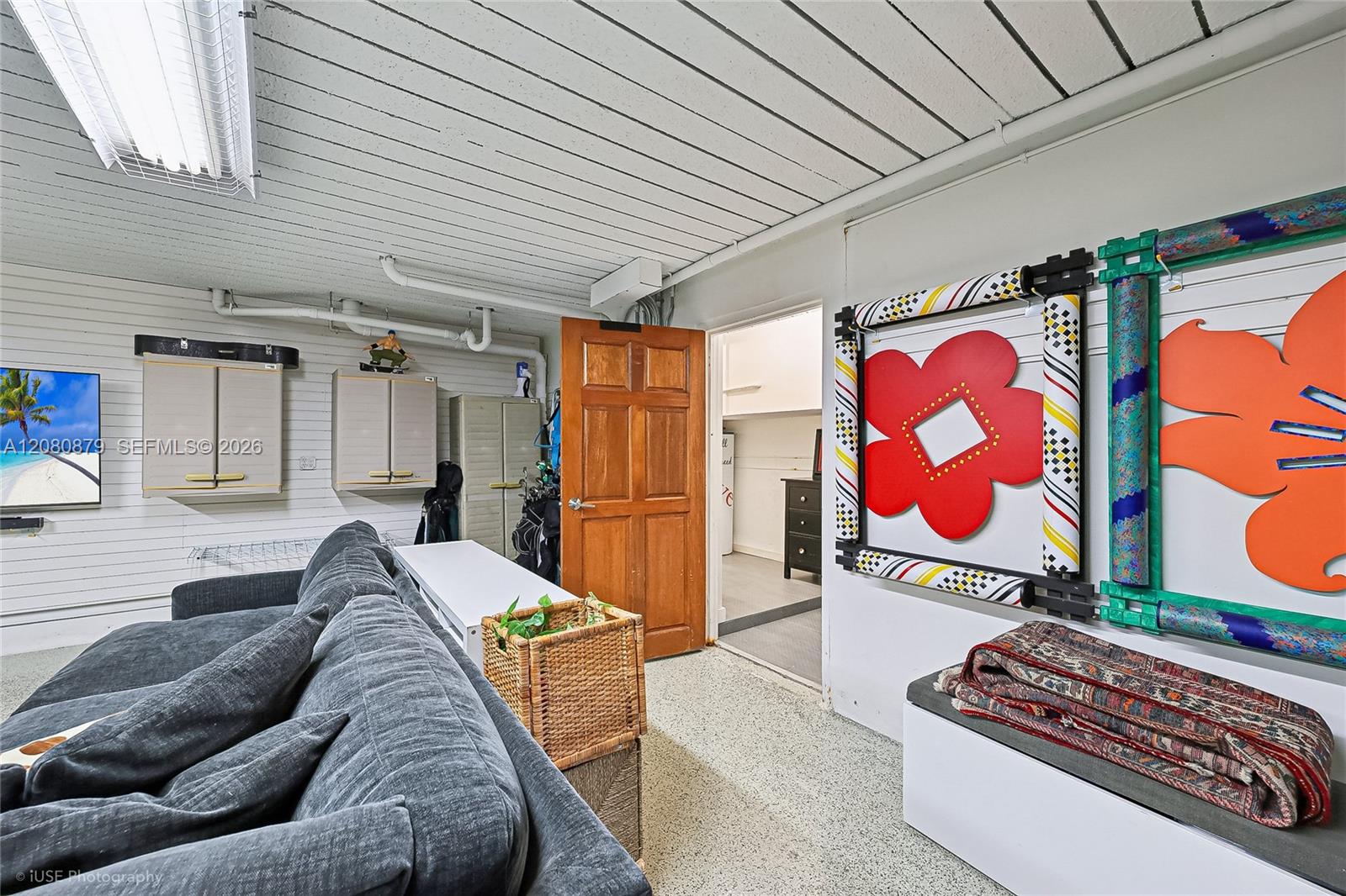 Furnished room with a gray sectional, storage cabinets, and colorful framed artwork.