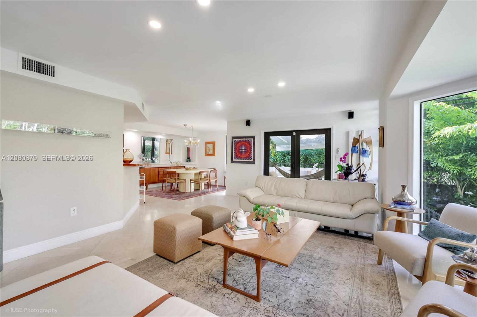 Furnished living room with white sofa, open dining area, and garden-facing glass doors.
