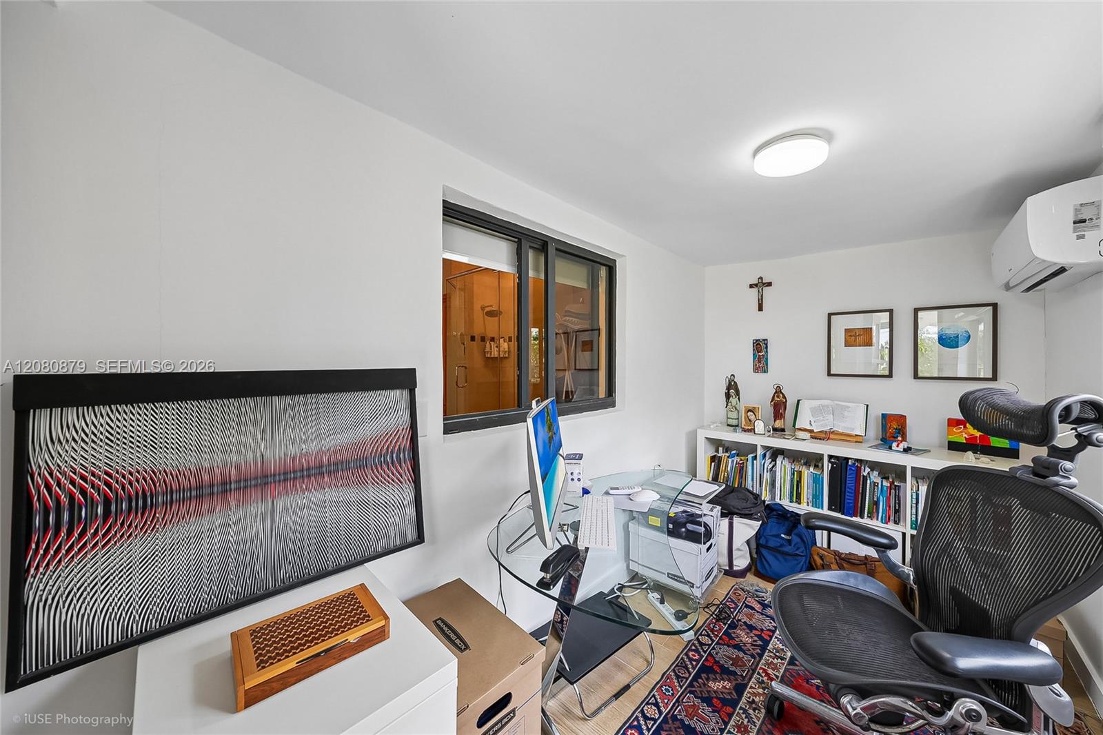 Home office with glass desks, office chairs, a bookshelf, and a patterned rug.