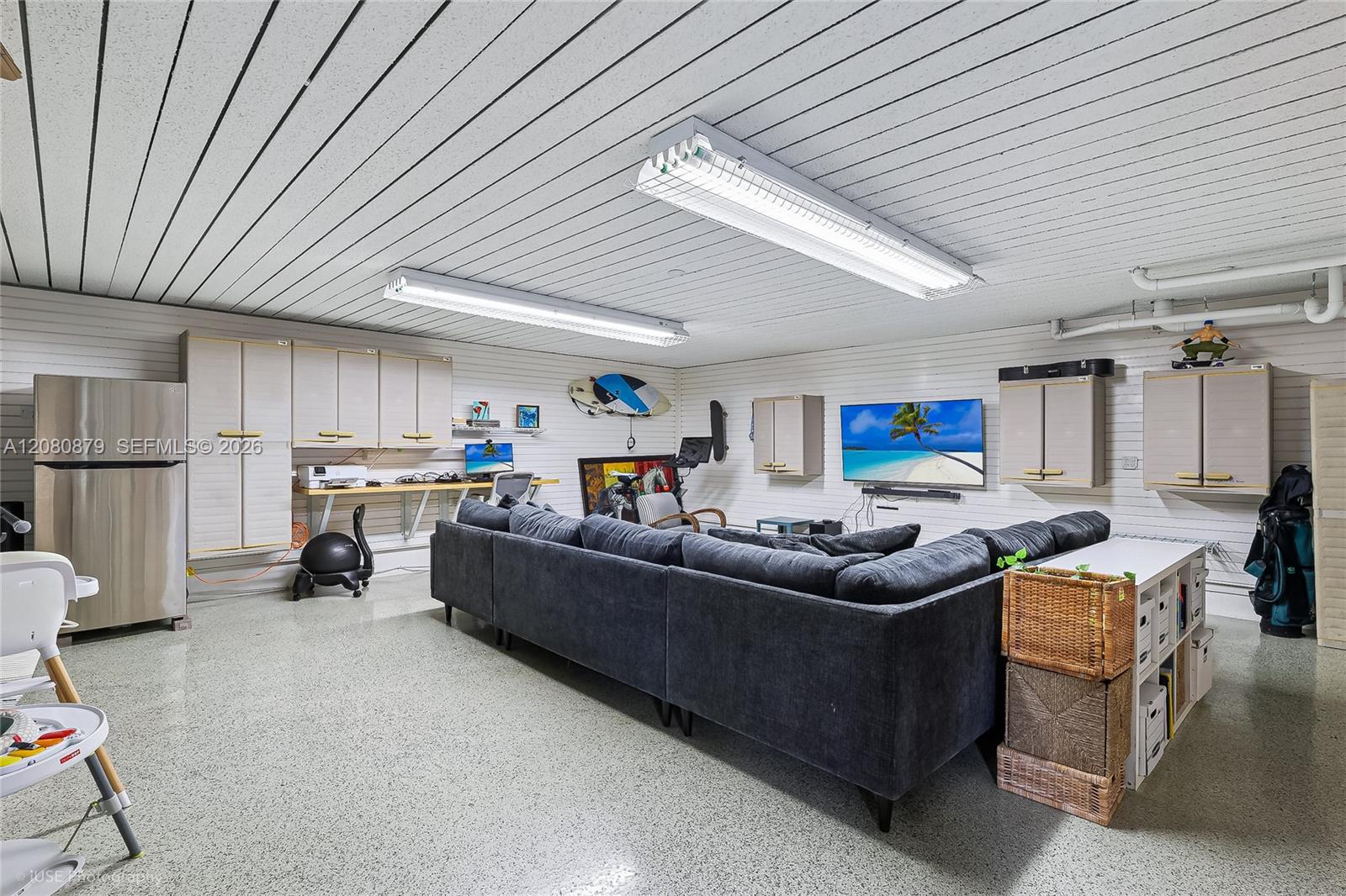 Furnished recreation room with a dark sectional sofa, wall cabinets, desk, and refrigerator.