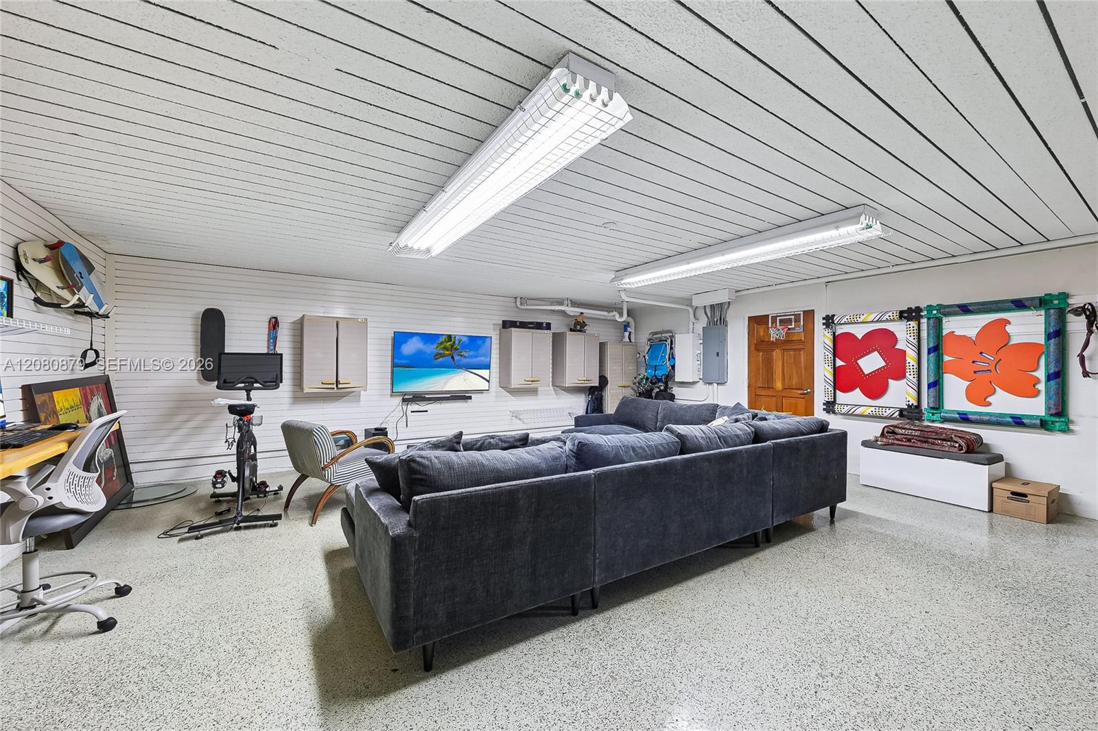 Furnished recreation room with a gray sectional, exercise bike, television, and colorful wall art.