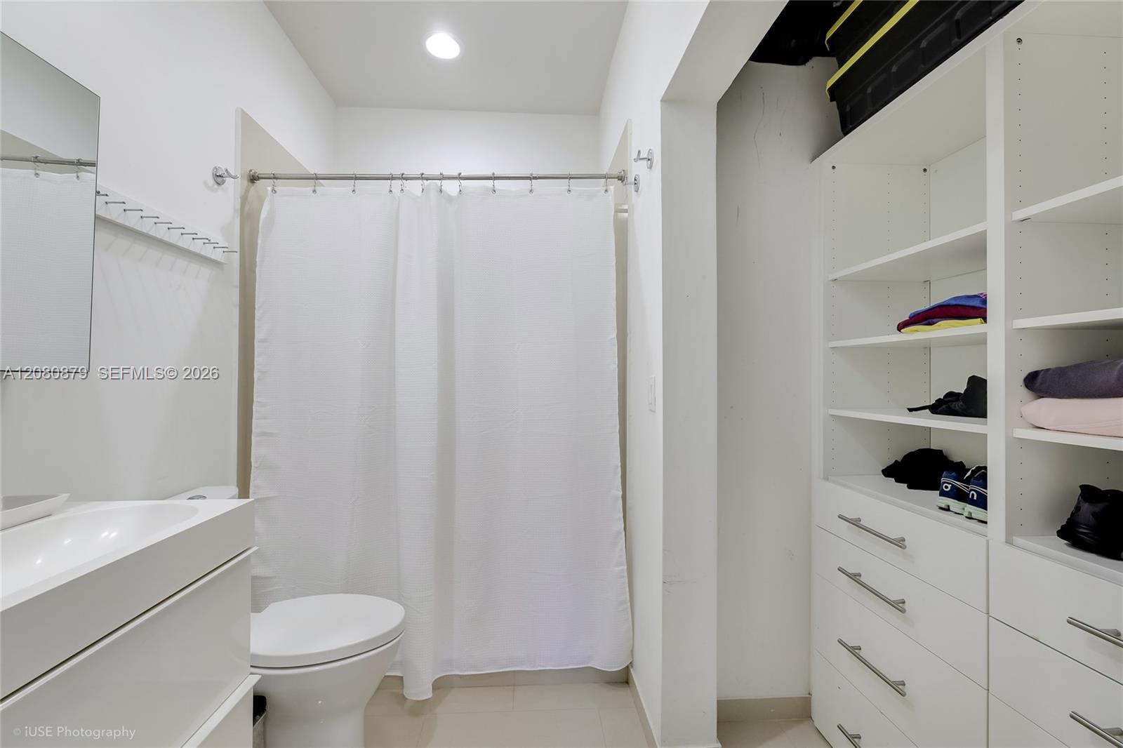 Bathroom with a white shower curtain and vanity beside built-in shelving and drawers.