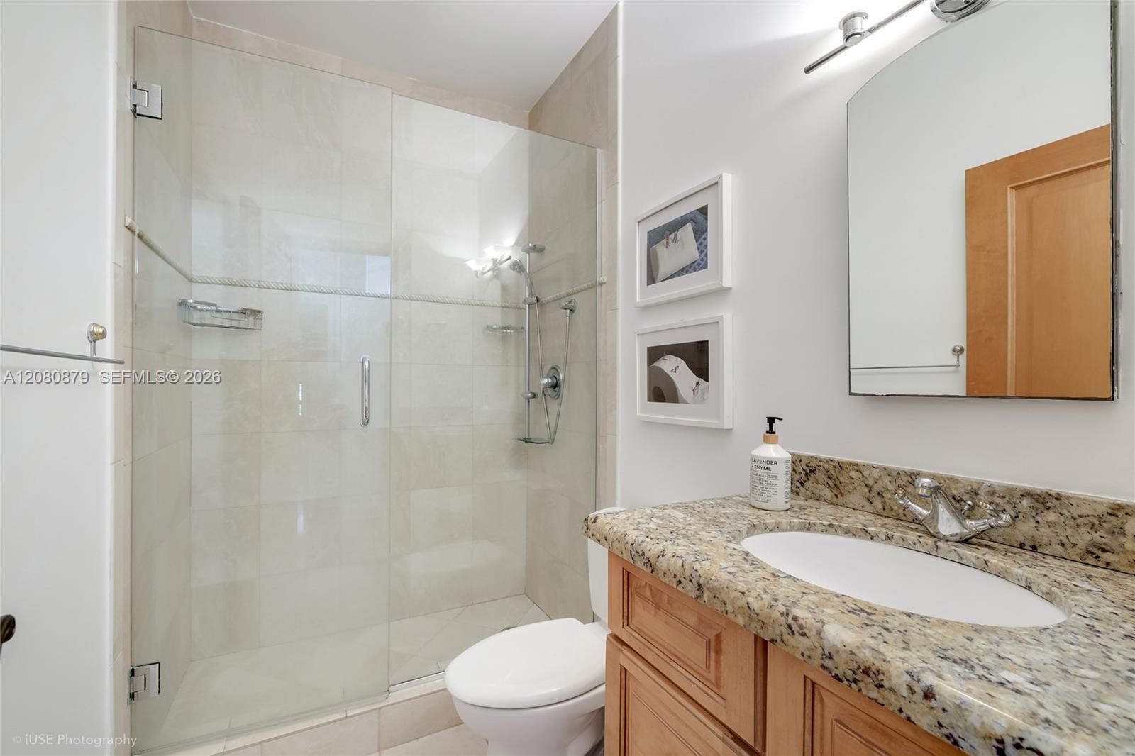 Bathroom with a glass-enclosed tiled shower and granite vanity with wood cabinetry.