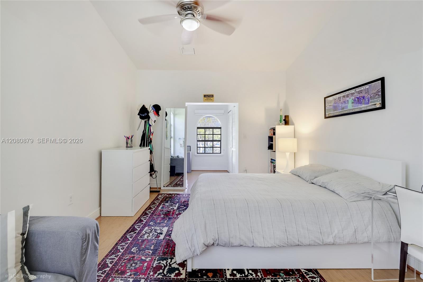 Bedroom with a large white bed, patterned rug, ceiling fan, and arched window.