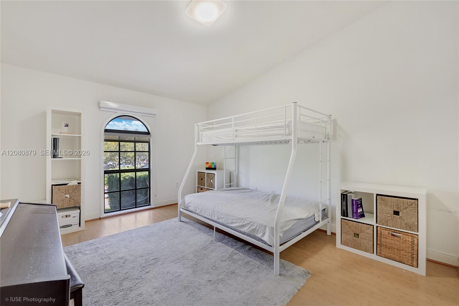 Bedroom with a white loft bunk bed, arched window, and built-in shelving.