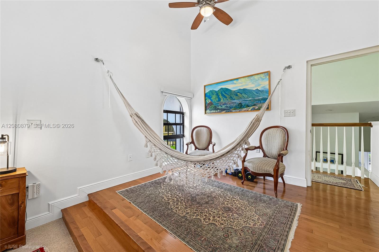 Upstairs sitting area with a hammock, two upholstered chairs, an arched window, and patterned rug.