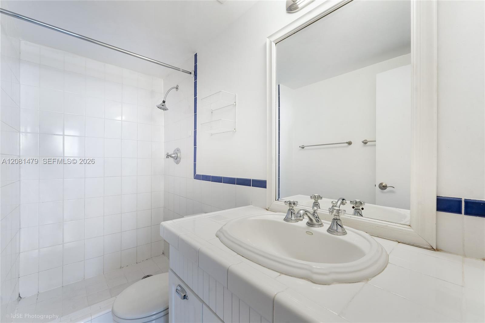 Bathroom with a white tiled shower, blue tile accents, and a built-in vanity beneath a large mirror.