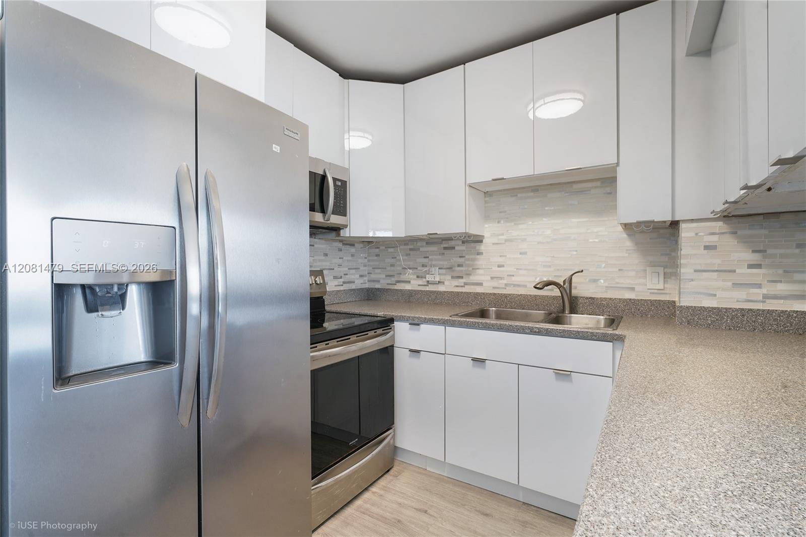 Kitchen with white cabinets, stainless appliances, mosaic backsplash, and double-basin sink.