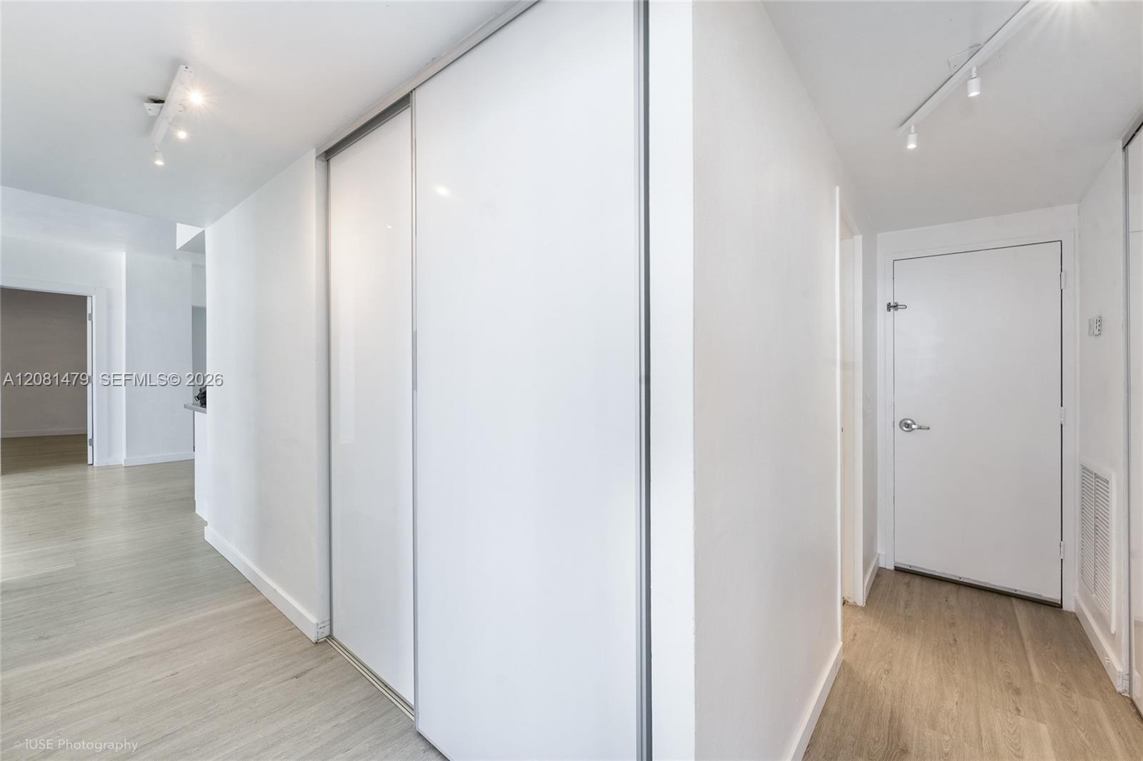 Apartment hallway with large sliding closet doors, a front entry door, and light wood-look flooring.