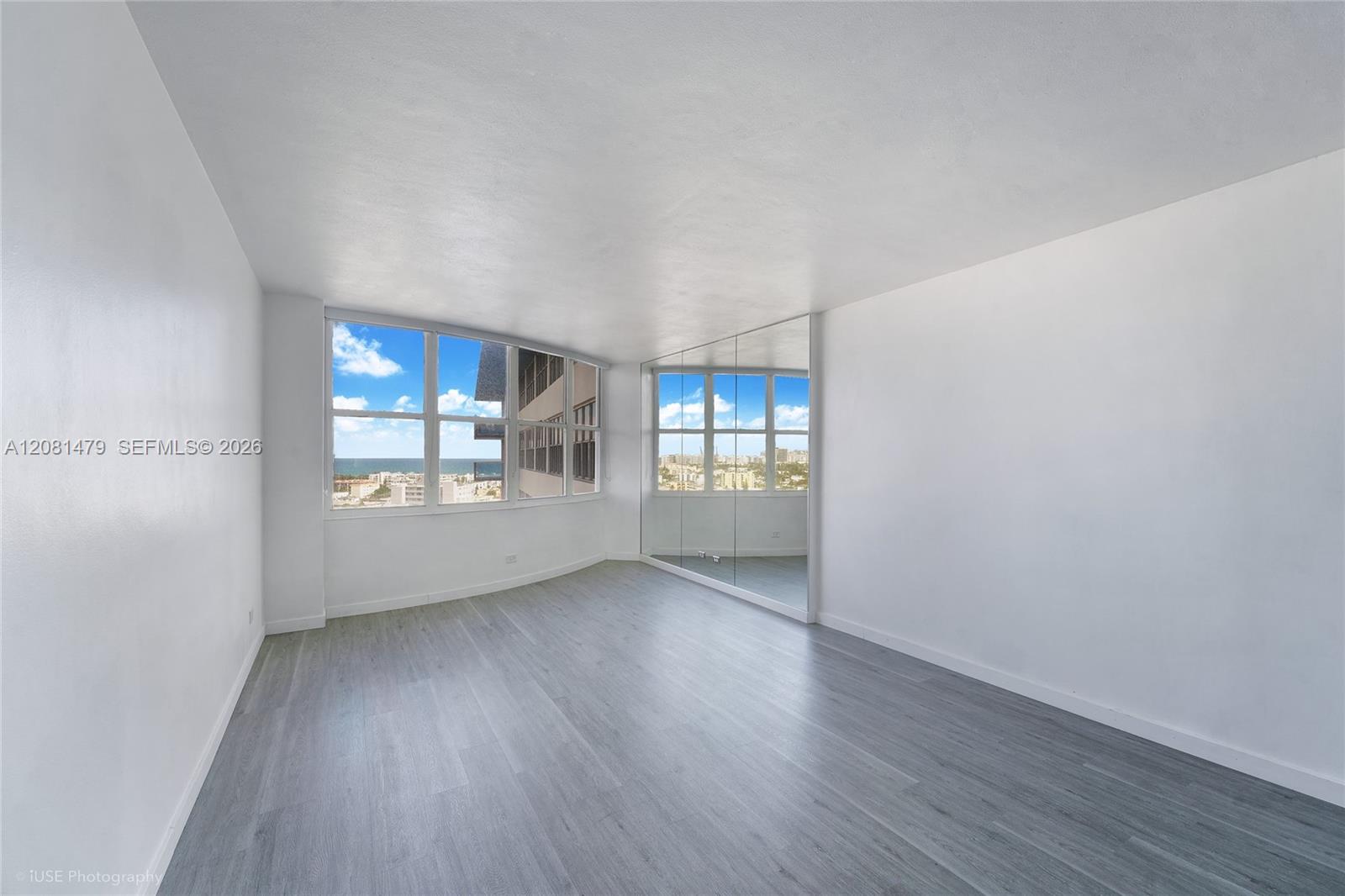 Vacant living room with gray flooring, mirrored wall, and large ocean-view windows.