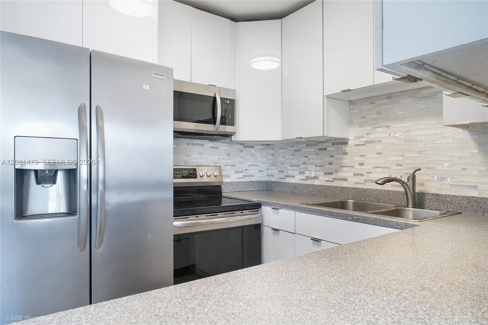 Modern kitchen with stainless-steel appliances, white cabinets, mosaic backsplash, and a double-basin sink.