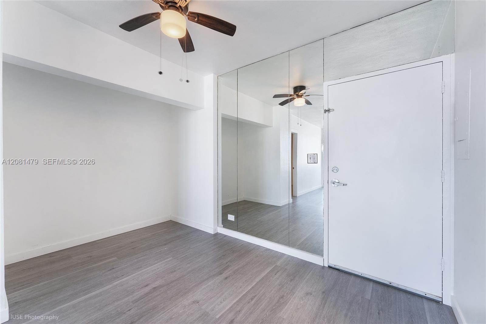 Empty interior with mirrored wall, gray plank flooring, white entry door, and ceiling fan.