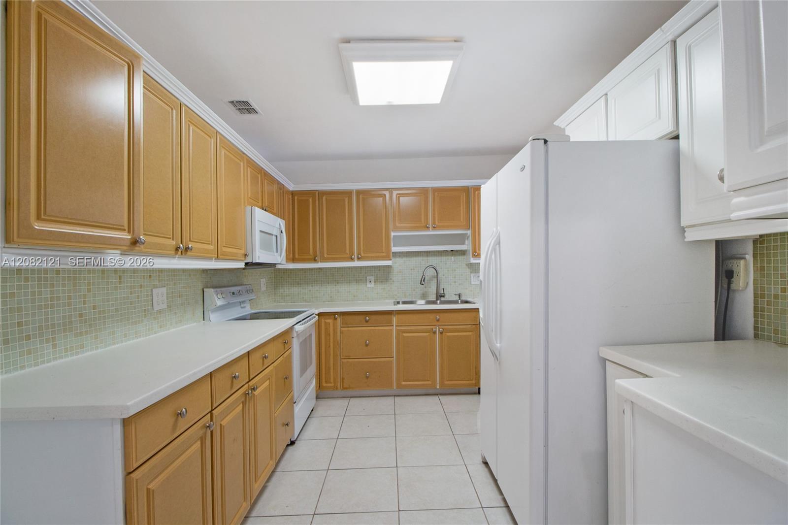 Kitchen with honey-colored cabinets, white appliances, and a pale green mosaic tile backsplash.